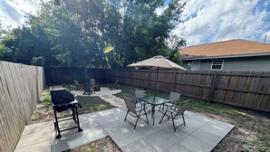 Un patio trasero con una parrilla, mobiliario exterior y una piscina.