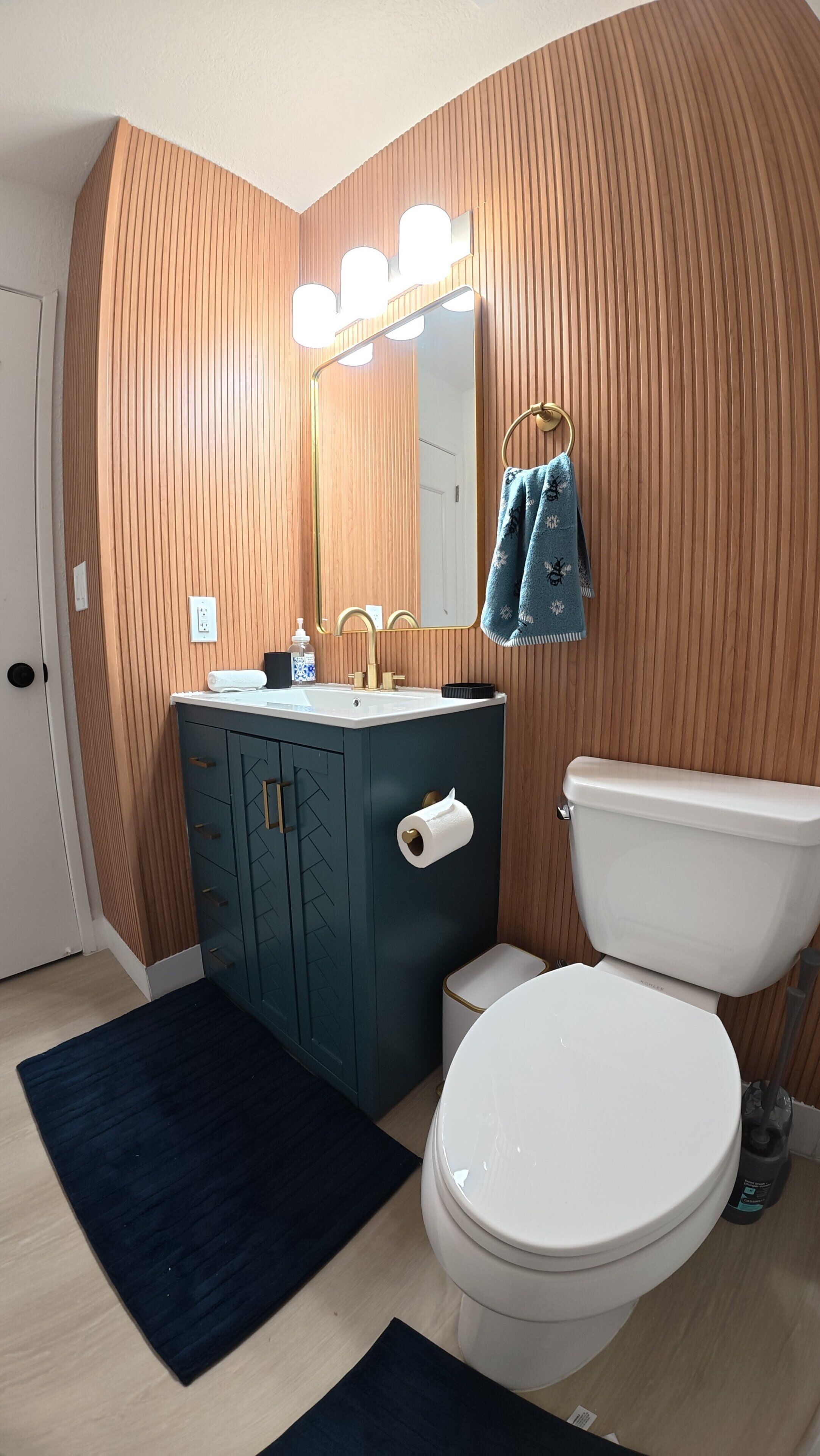 Ein Badezimmer mit Holzwand, Waschbecken mit Spiegel, Toilette und einem dunkelblauen Teppich.