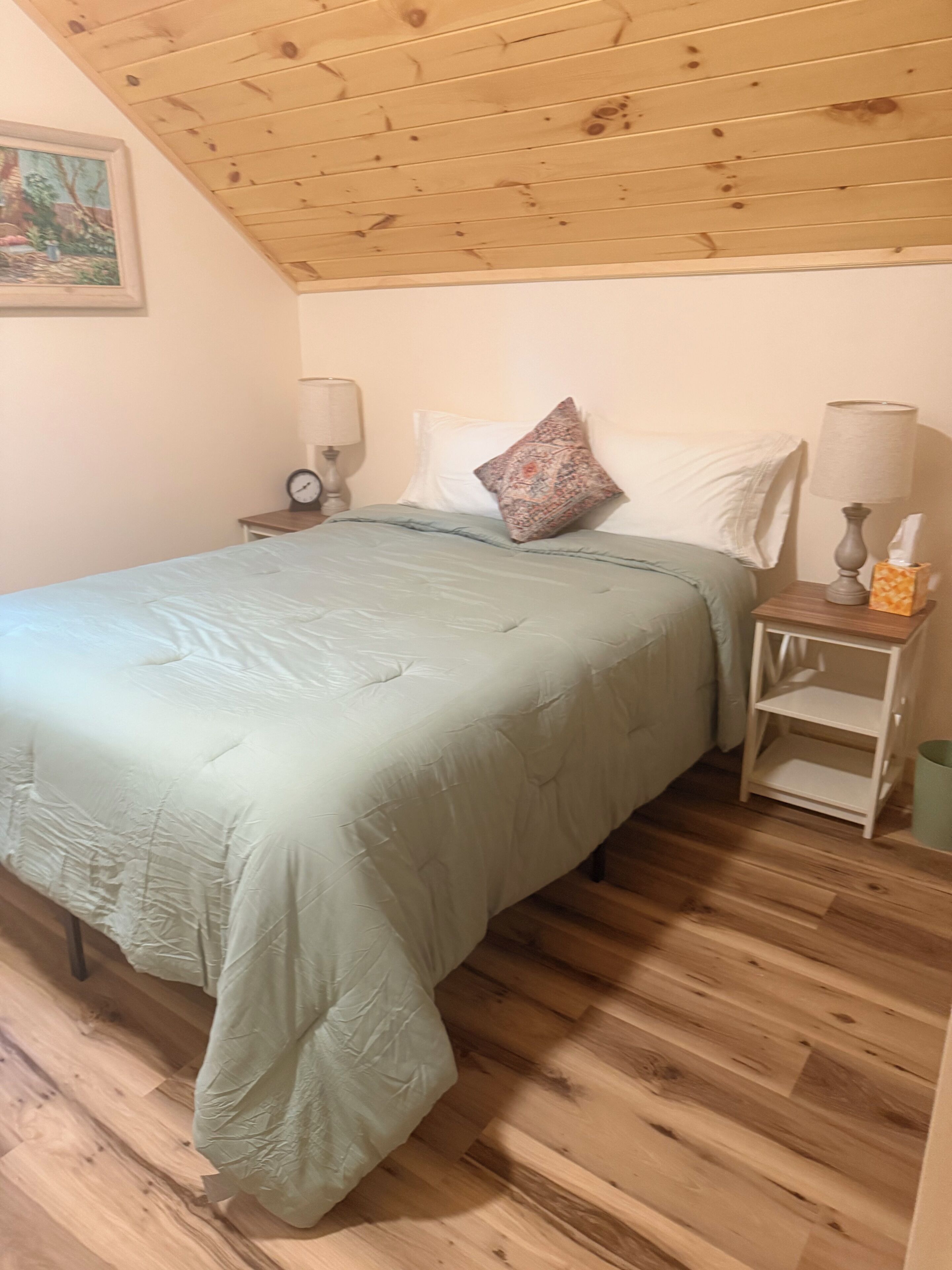 Une chambre à coucher comprenant un lit, deux tables de chevet, une commode, une lampe, une horloge et un tableau accroché au mur.