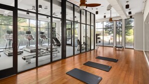 A spacious gym with exercise equipment, large windows, and wooden flooring.