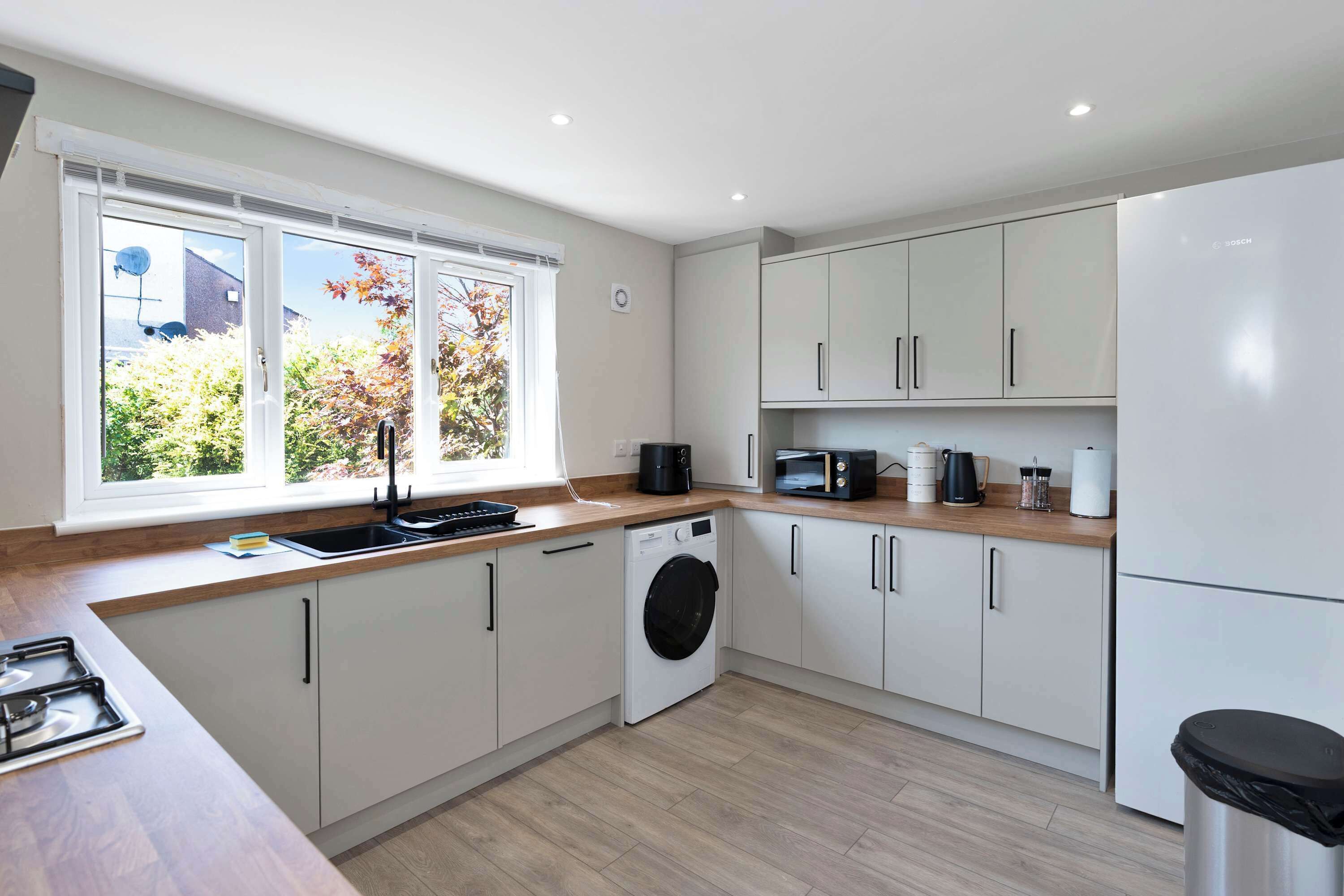 A modern kitchen with a washing machine, microwave, and a large window.