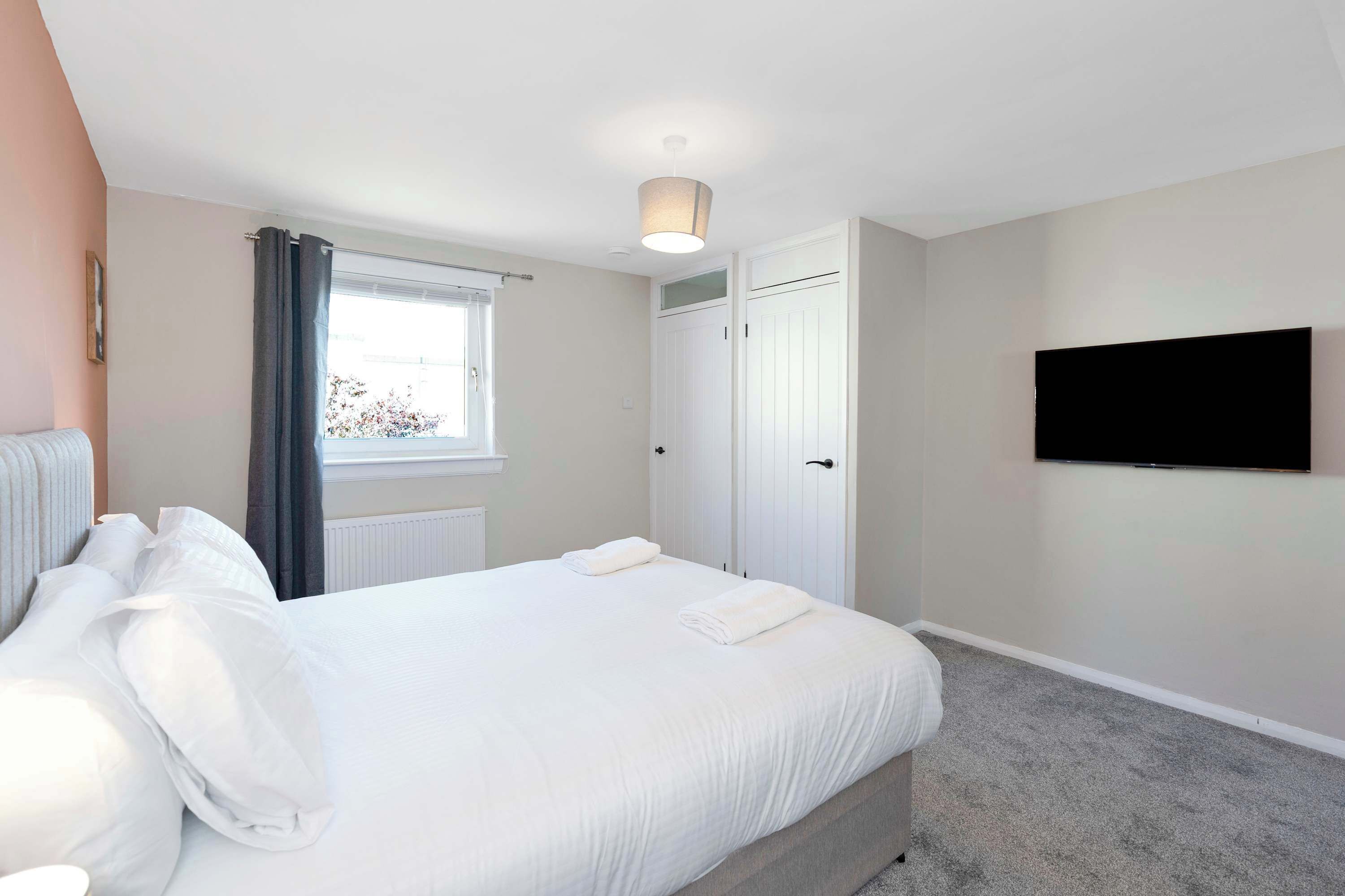 Een slaapkamer met een bed, een televisie, een raam met gordijnen en een radiator.
