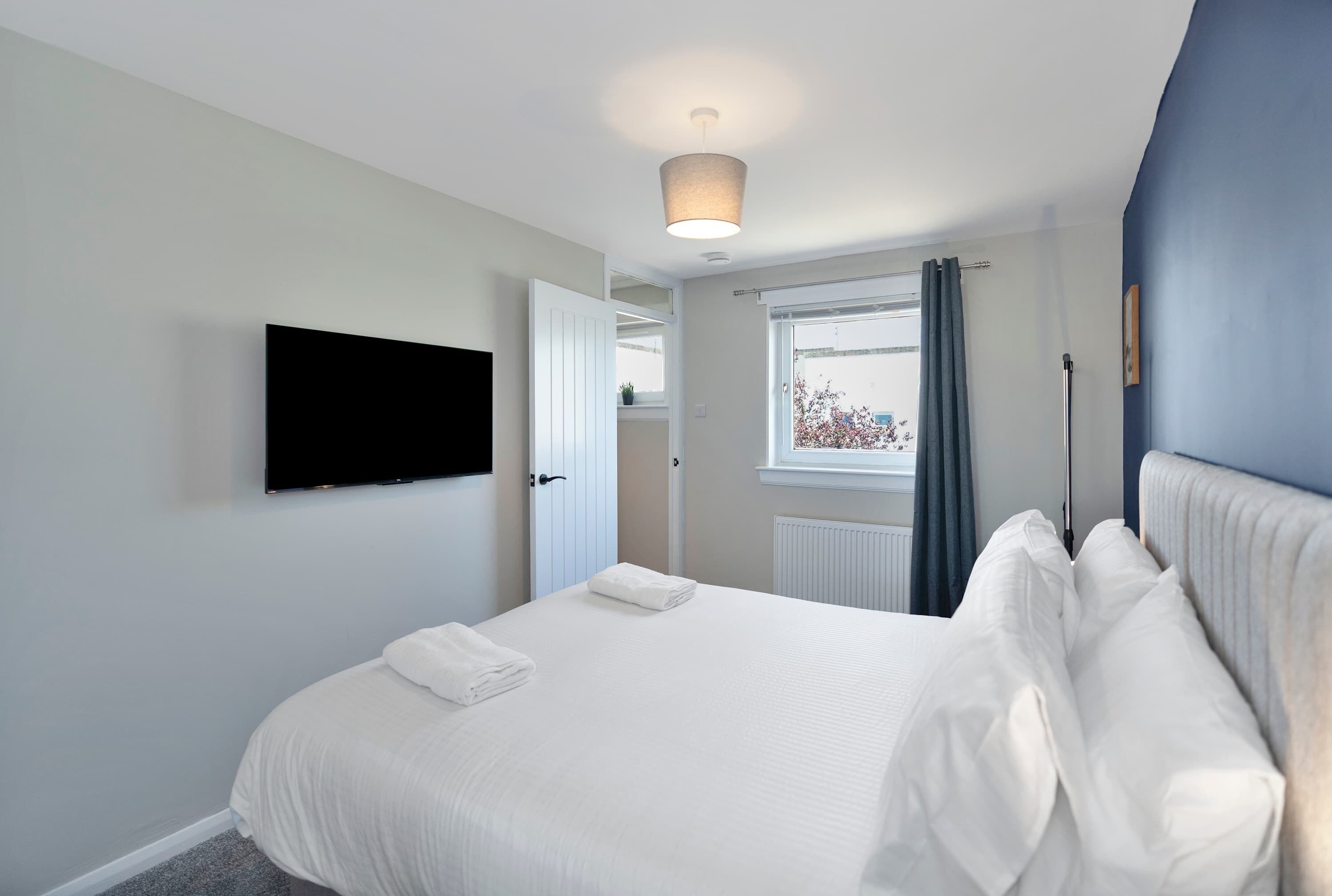 Una camera d'albergo con un letto, una televisione a schermo piatto, una finestra con tende e un termosifone.
