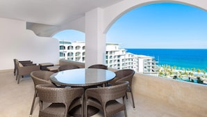 A round table with wicker chairs on a balcony overlooking a beach and hotel buildings. - Luxury Ocean Front Suite (San José del Cabo)