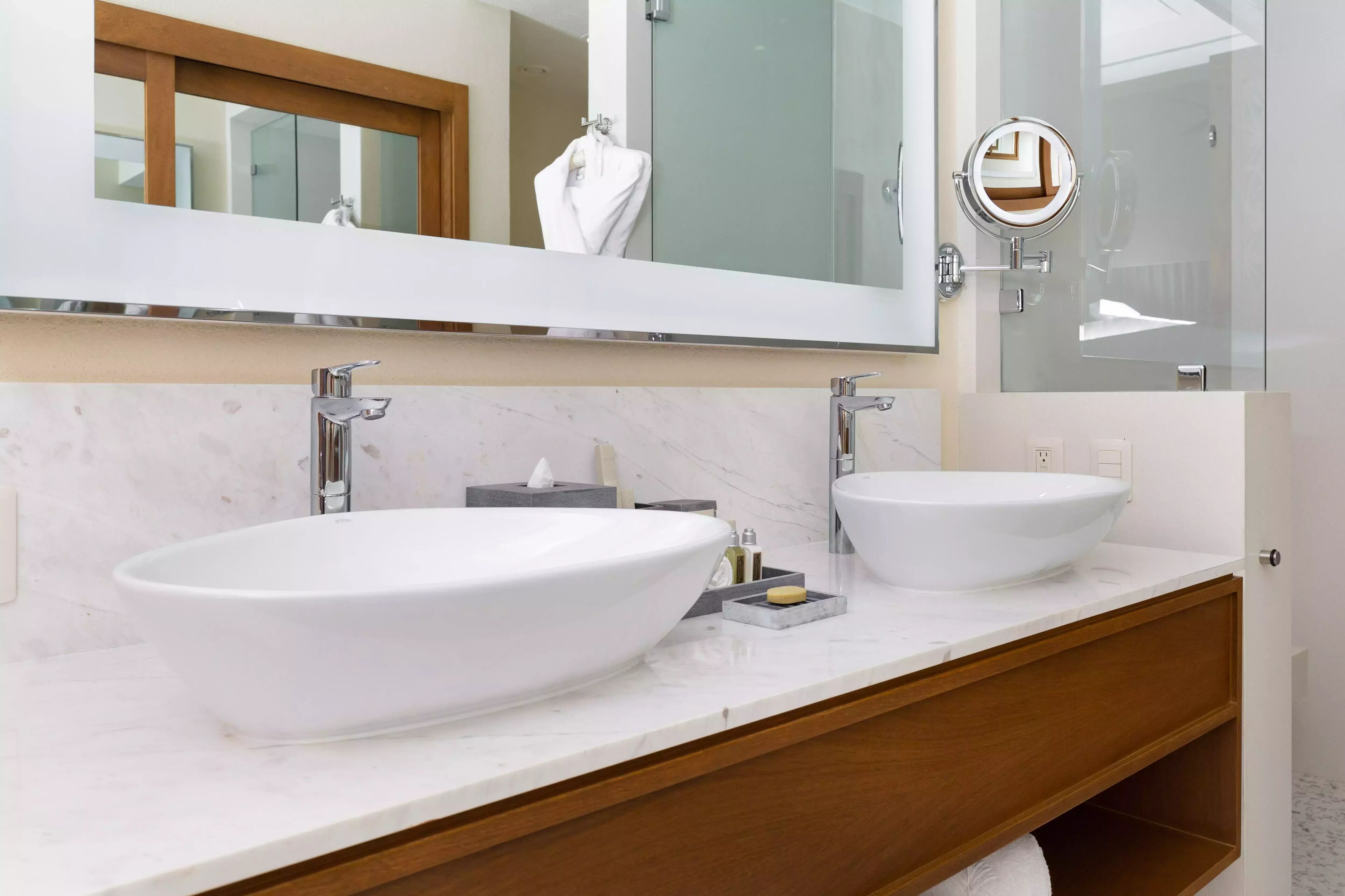 A modern bathroom with two large white sinks, a large mirror, and a wooden vanity.