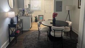 A dining area with a round table, four chairs, a lamp, a small potted plant, and a kitchen in the background. - The Buckhead Luxe – by Vivo (Atlanta)