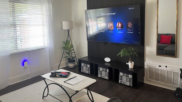 A modern living room with a flat-screen TV, a standing lamp, a coffee table, and a sofa with a red cushion. - The Buckhead Luxe – by Vivo (Atlanta)