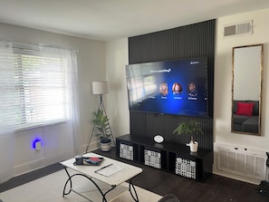 A modern living room with a flat-screen TV, a standing lamp, a coffee table, and a sofa with a red cushion.