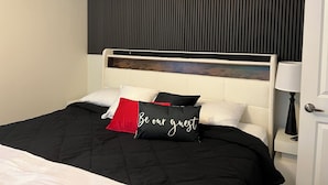 A hotel room with a bed, a headboard, a bedside table with a lamp, and a door. - The Buckhead Luxe – by Vivo (Atlanta)