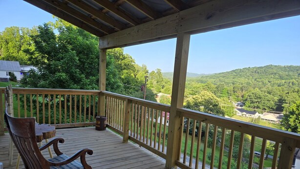 A wooden deck with a rocking chair and a table, overlooking a forested landscape. - Cozy 1-bedroom house with a beautiful view from the large deck (ansted)