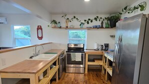 A compact kitchen with wooden countertops, stainless steel appliances, and a window overlooking greenery. - Cozy 1-bedroom house with a beautiful view from the large deck (ansted)