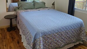 A bedroom with a bed, a ceiling fan, a window with curtains, a small table, and a mirror. - Cozy 1-bedroom house with a beautiful view from the large deck (ansted)