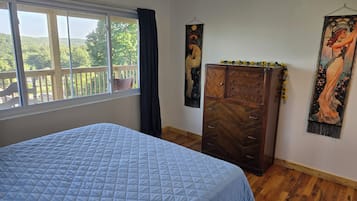 A bedroom with a bed, a wooden dresser, a window with a view, and two wall hangings.