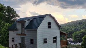 A two-story house with a metal roof, a front porch, and a small deck. - Cozy 1-bedroom house with a beautiful view from the large deck (ansted)