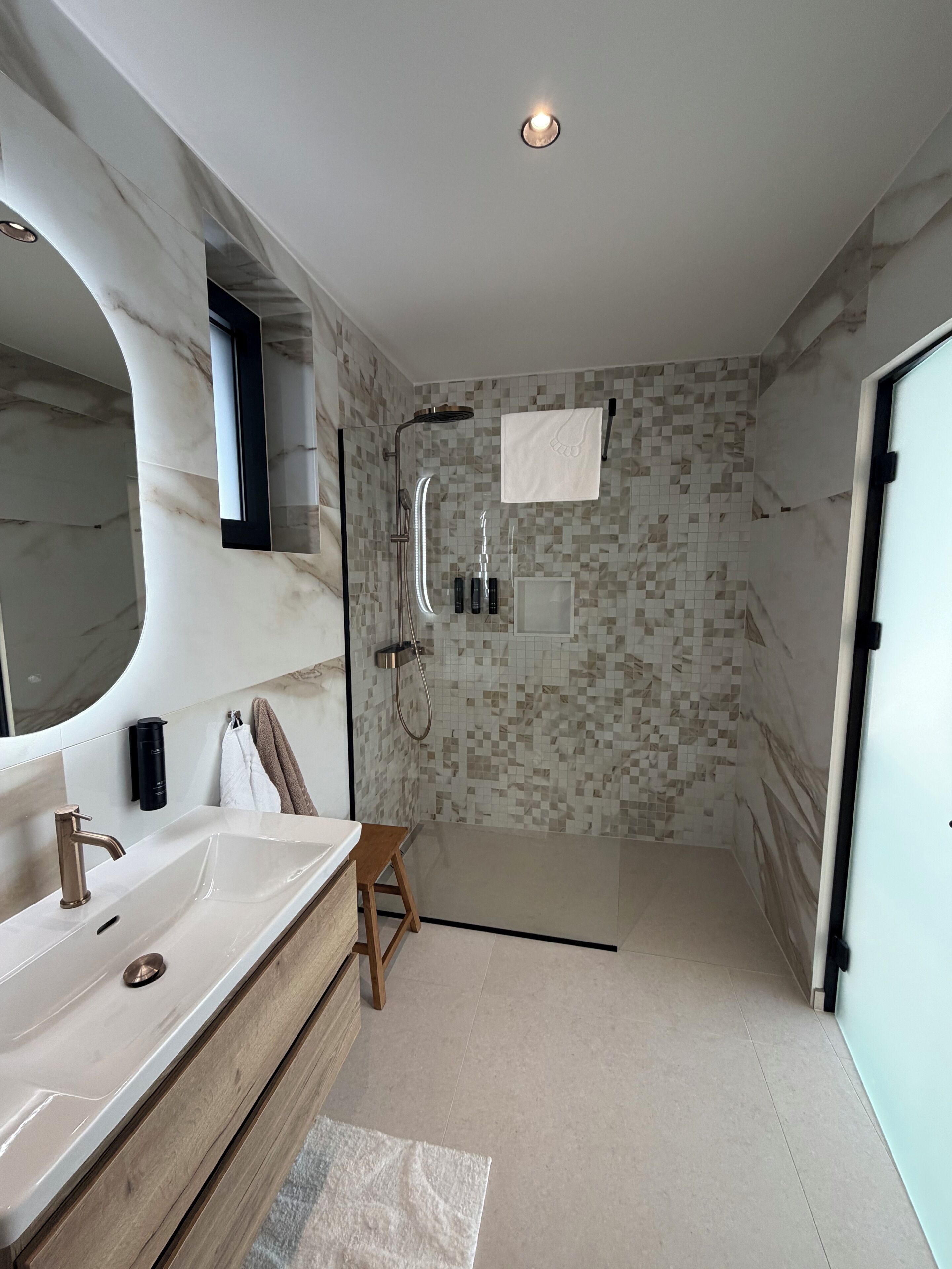 Un bagno moderno con uno specchio grande, un lavandino, una doccia e un porta asciugamani.