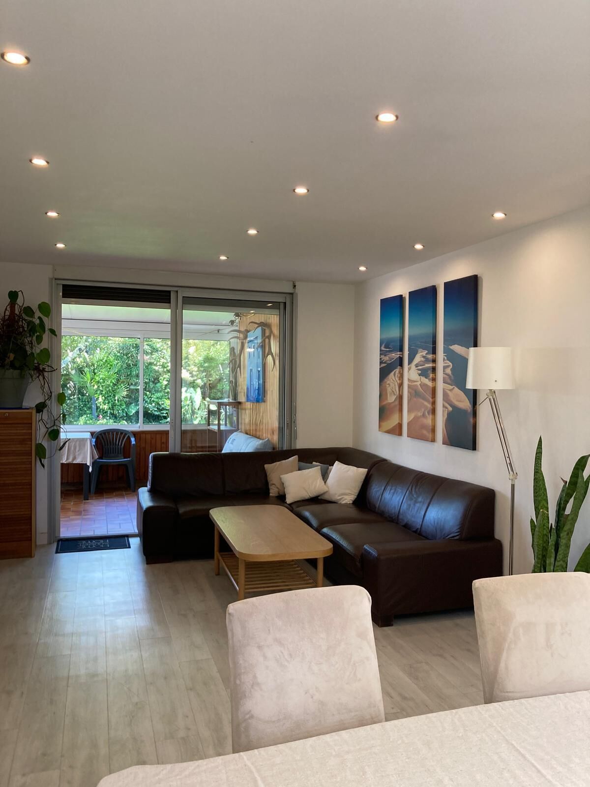 A modern living room with a sofa, a coffee table, and a lamp. There are three paintings on the wall and a plant on the right.