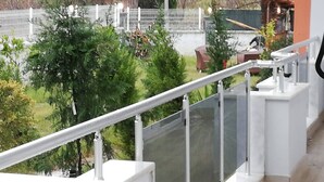 A balcony with a white railing overlooking a garden with trees and a fence. - Apartment in Side Evrenseki, Hotel Comfort Home Feel (Manavgat)