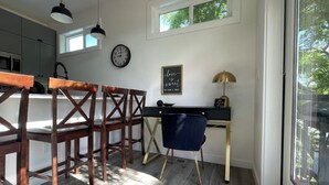 Ein Essbereich mit Holzkreisen und Tisch, ein Schreibtisch mit Stuhl, eine Uhr und ein Fenster mit Blick auf Bäume.