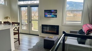 Ein Wohnzimmer mit Kamin, Wandfernseher und großem Fenster.