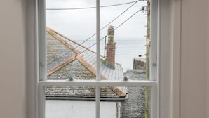 Une fenêtre donnant sur un bâtiment situé sur la côte, avec une cheminée en briques et un toit recouvert de tuiles.