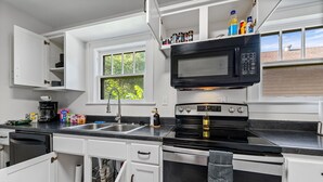 A kitchen with white cabinets, a black microwave, a stove, and a window with a view of greenery. - Independence House Near GEHA Field & Fenced Yard (Independence)