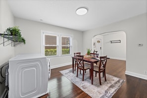 Uma área de refeições com mesa, cadeiras, tapete e um eletrodoméstico branco.