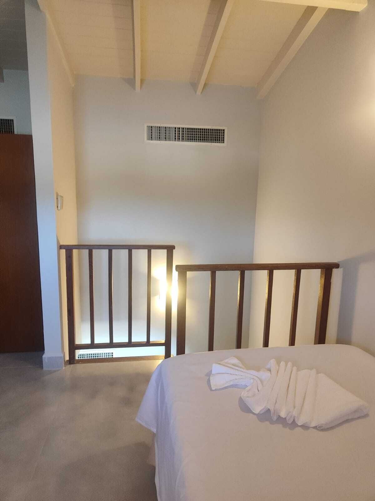 A bedroom with a bed, a wooden headboard, a white wall, a vent, and a door.