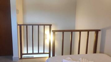 A bedroom with a bed, a wooden headboard, a white wall, a vent, and a door.