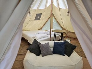 Une tente équipée d’un lit, d’une petite table et d’un espace salon avec des coussins.