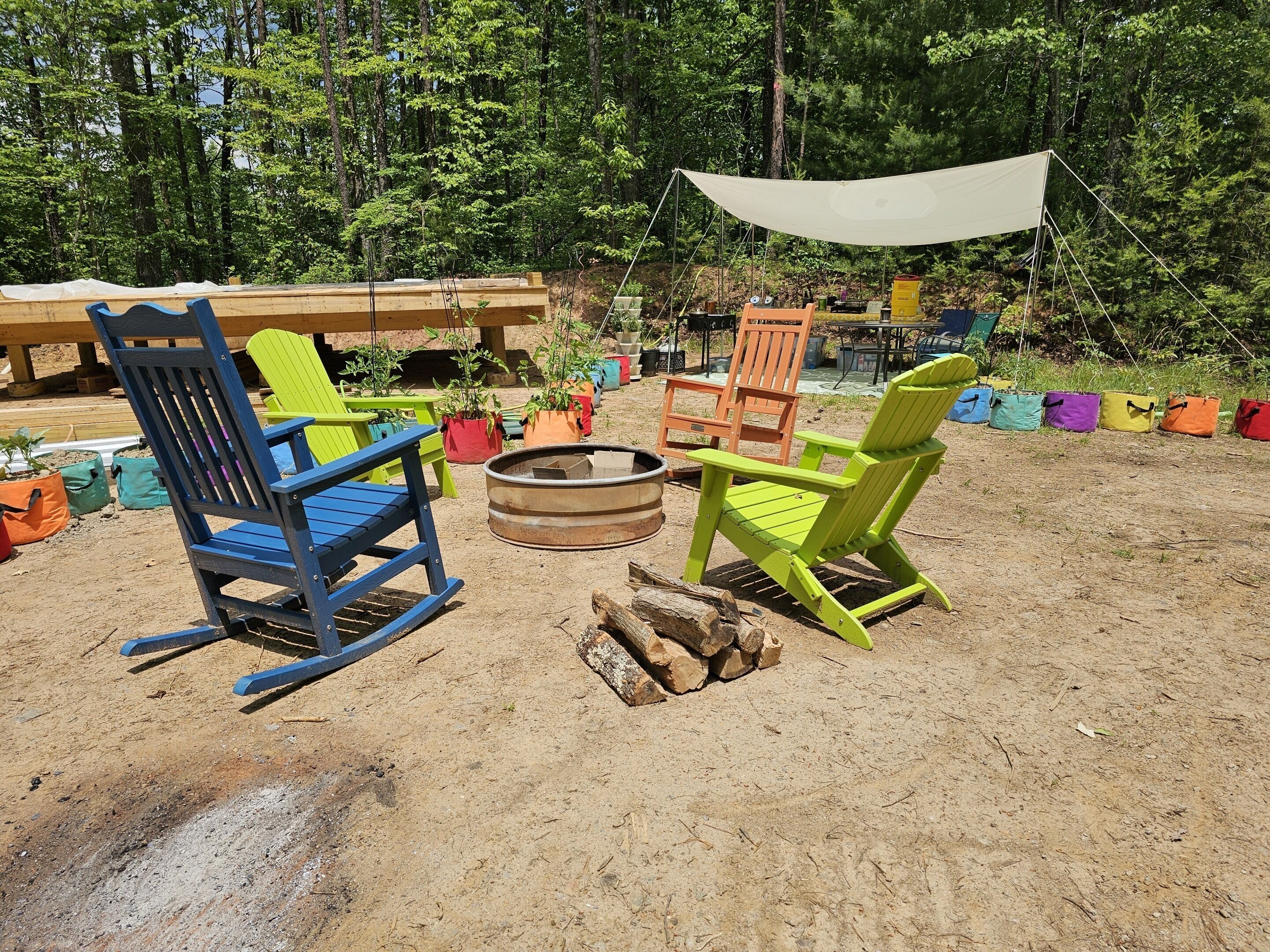 Een camping met twee Adirondack stoelen, een vuurkuil en een luifel.