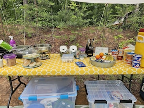 Un espace de camping aménagé avec une table pour les repas, une glacière et des récipients de rangement.