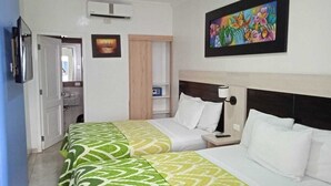 A hotel room with two beds, a bedside table with a lamp, a painting on the wall, and an air conditioning unit.