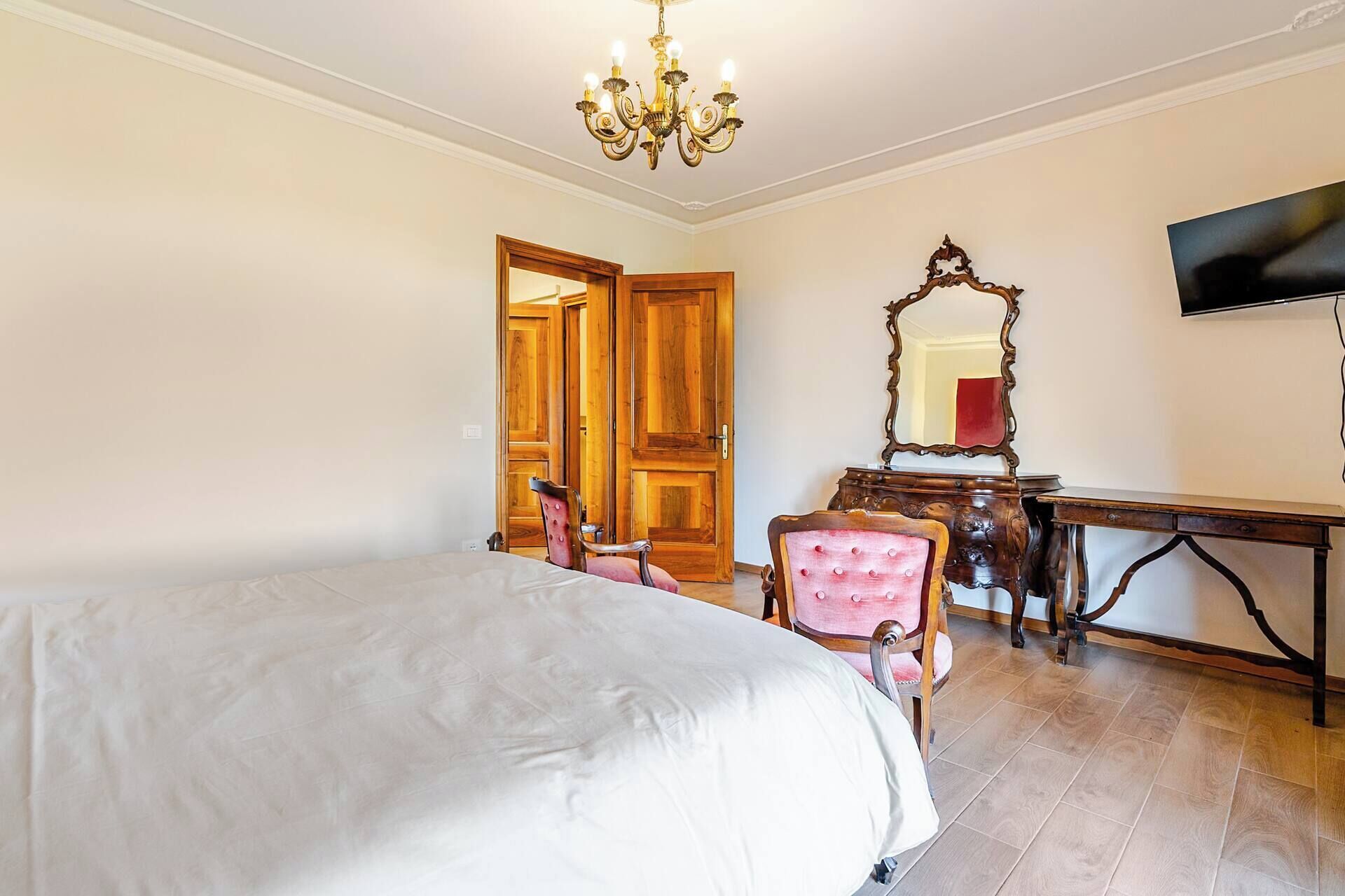 Ein Schlafzimmer mit einem Bett, einem Sessel, einem Holztisch, einem Spiegel und einem an der Wand befestigten Fernseher.