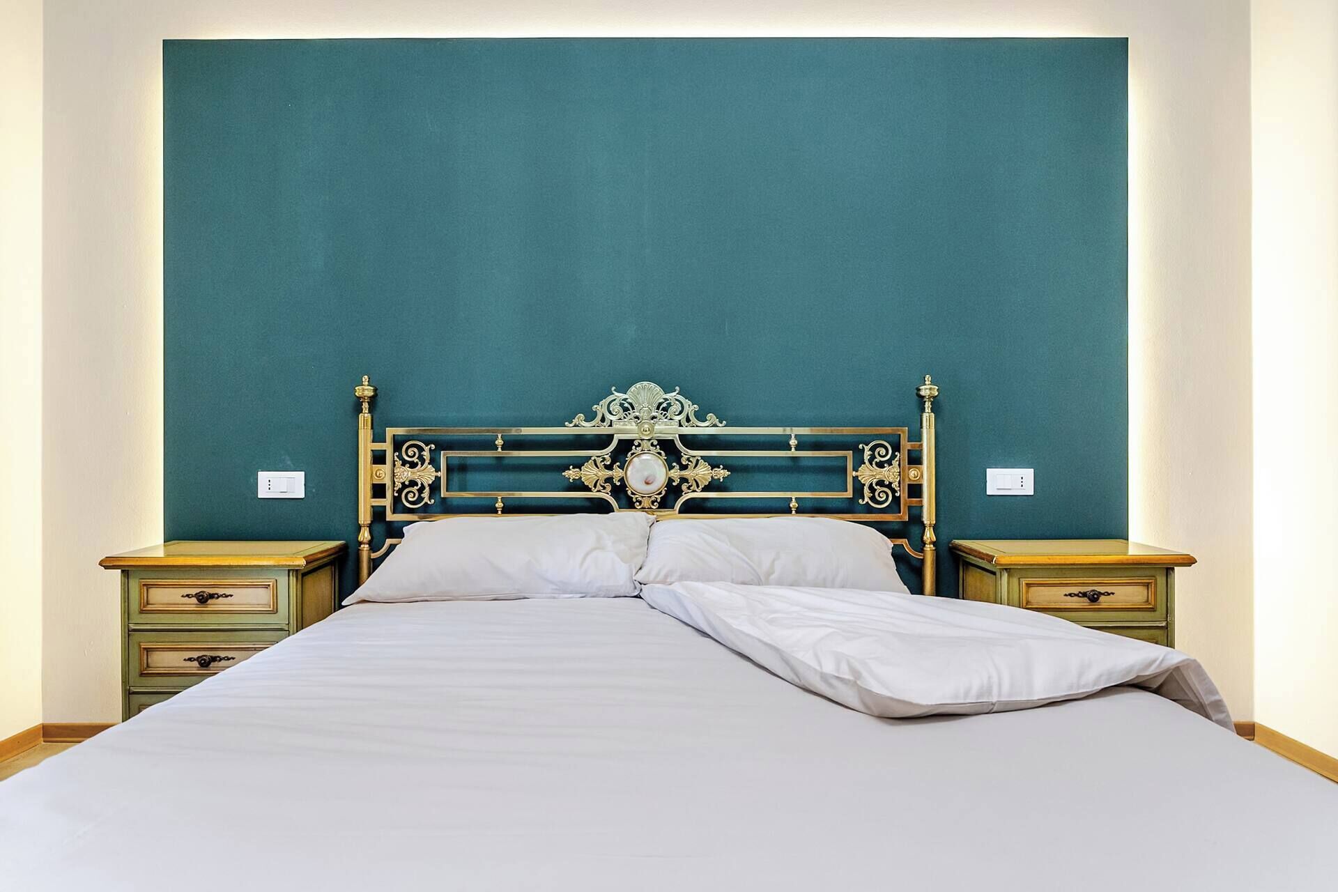 Ein Bett mit ornamentalem Kopfteil, zwei Nachttische und eine grüne Wand.