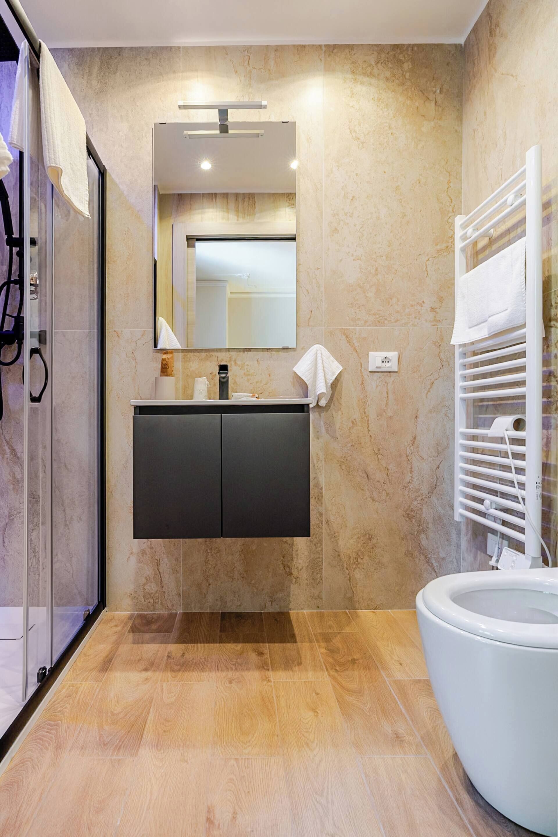 A modern bathroom with a glass shower enclosure, a dark vanity, a large mirror, and a white bathtub.