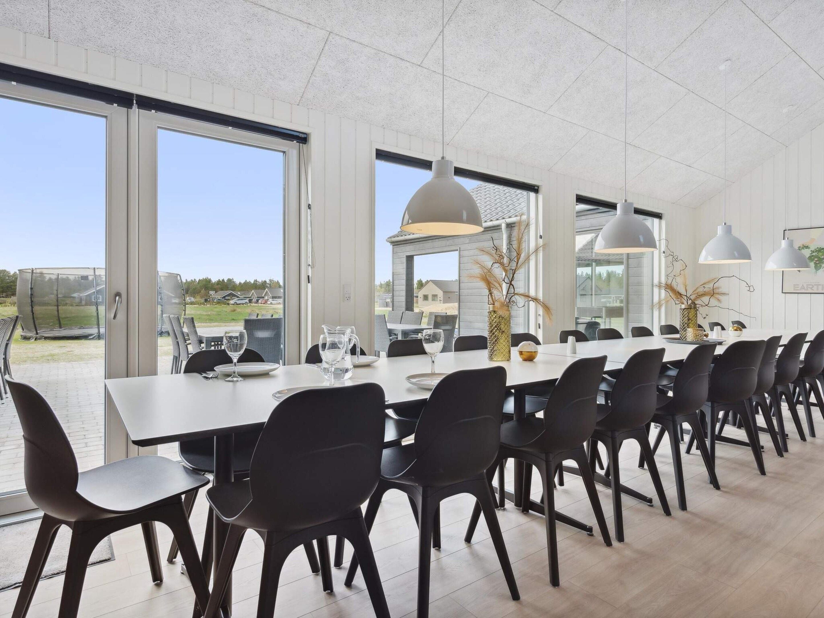 A modern dining area with a long table, black chairs, and large windows offering a view of the outdoors.