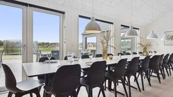 Et moderne spiseområde med et langt bord, sorte stole og store vinduer med udsigt til naturen.