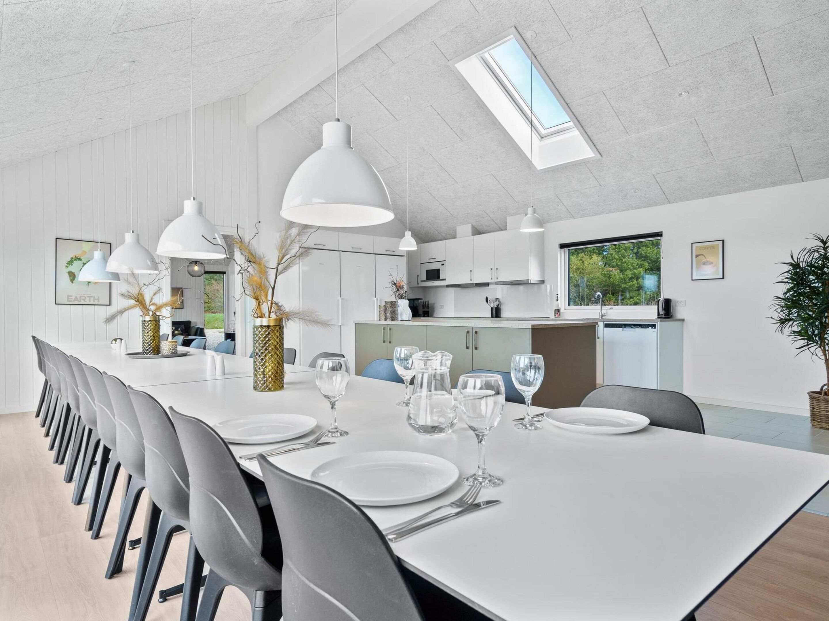 Un espace de salle à manger moderne, avec une longue table, de nombreuses chaises et des luminaires suspendus.
