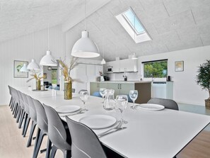A modern dining area with a long table, multiple chairs, and pendant lighting. - 5 Star Holiday Home in Norre Nebel (Norre Nebel)