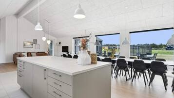 Et moderne køkken med en stor ø, hængende lamper og udsigt til det fri.