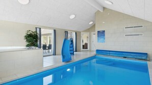 An indoor swimming pool with a blue slide, a seating area, and a door leading to an adjacent room. - 5 Star Holiday Home in Norre Nebel (Norre Nebel)