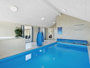Una piscina interior con un tobogán azul, una zona de estar y una puerta que da a una habitación contigua.