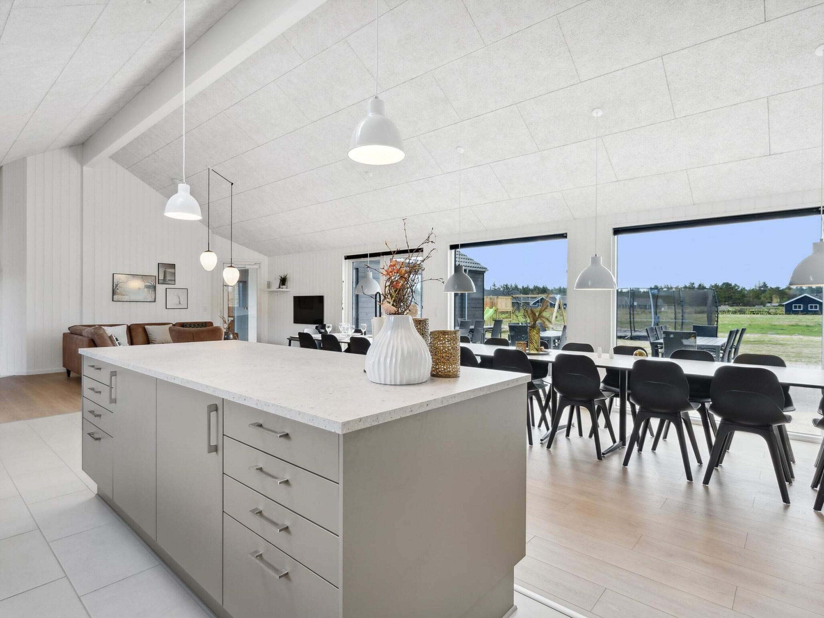 Une cuisine moderne dotée d’un grand îlot central, de luminaires suspendus et offrant une vue sur l’extérieur.