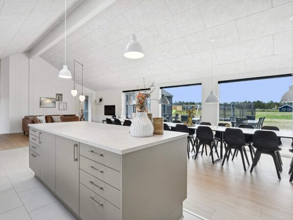 Una cocina moderna con una isla grande, iluminación colgante y vistas al exterior.