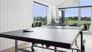A modern room with a ping pong table, large windows, and a view of a green landscape. - 5 Star Holiday Home in Norre Nebel (Norre Nebel)