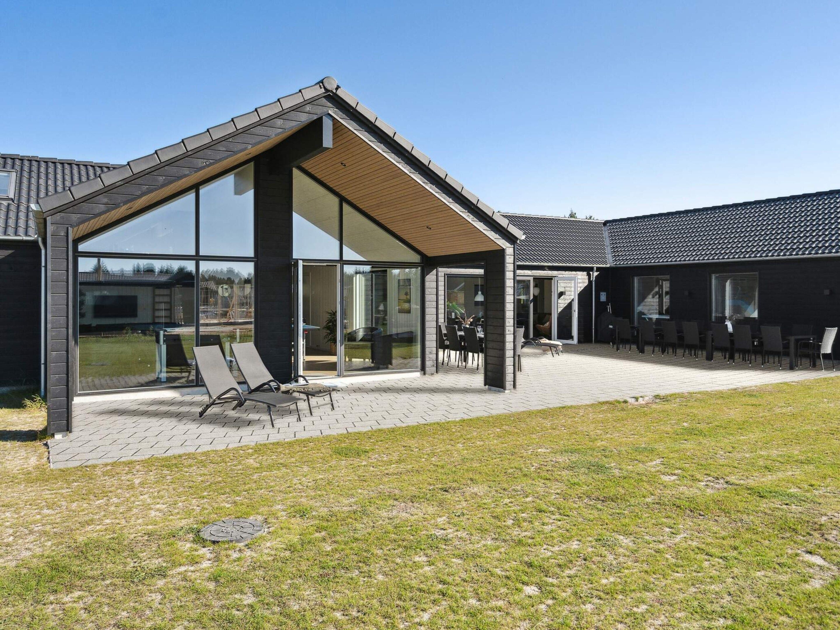 Un bâtiment moderne doté d’un patio couvert, de grandes fenêtres et d’un espace extérieur aménagé pour s’asseoir.