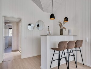 A modern kitchen with white wooden paneling, a bar area with stools, and pendant lighting. - 5 Star Holiday Home in Norre Nebel (Norre Nebel)