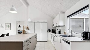 A modern kitchen with white cabinetry, a large island, and a window providing natural light. - 5 Star Holiday Home in Norre Nebel (Norre Nebel)