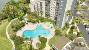 Edifício residencial com piscina, rodeado por vegetação e área de estacionamento.