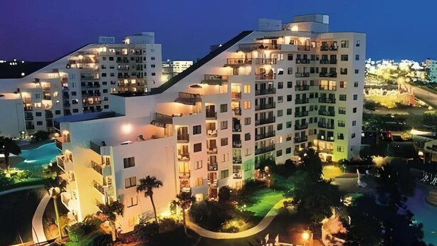 Um hotel com vários andares, varandas, piscina e jardins bem cuidados.